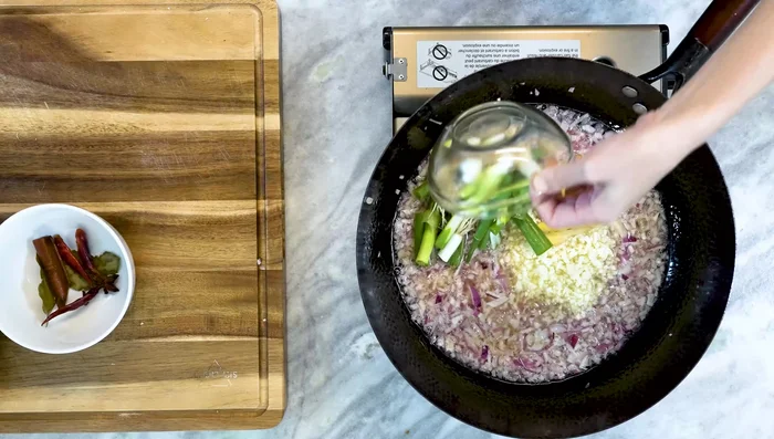 Add garlic, ginger, scallions, and soaked spices to the wok. Stir constantly and simmer for 20-30 minutes, or until golden brown.