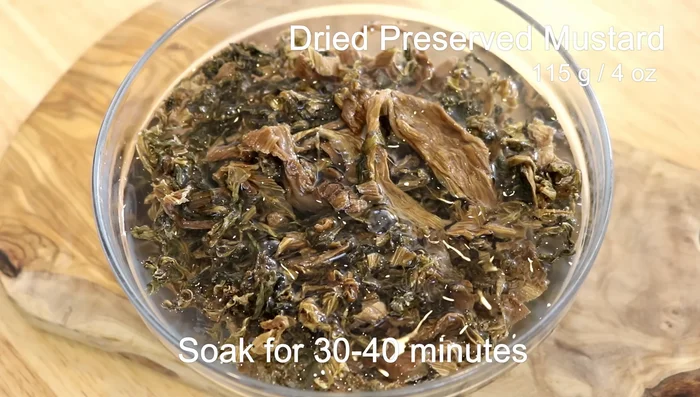 Prepare the Mei Cai (preserved mustard greens): Soak in room temperature water for 30-40 minutes. Drain, squeeze out excess water, and then stir-fry with oil, garlic, ginger, cinnamon, star anise, and dried orange peel (or fresh orange peel). Add leftover pork broth and adjust seasoning.
