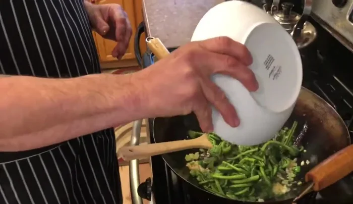 Add the boiled fiddleheads to the wok and stir-fry until coated with the garlic and oil.
