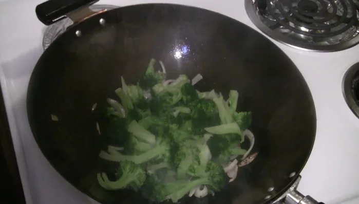 Add blanched broccoli to the wok and stir-fry.