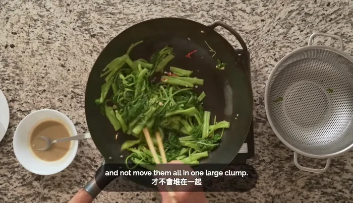 Add the blanched water spinach to the wok on high heat (657.88). Stir-fry quickly for about 1 minute to prevent burning (660.399).