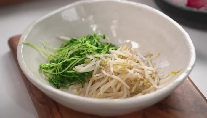 Combine ingredients: In a large bowl, toss together the cooled noodles, blanched vegetables, dressing, shredded chicken, and a portion of the toppings.