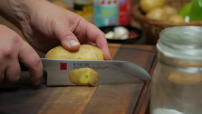 Wash potatoes. Cut a small slice from one side for stability. Using a fork to help, carefully slice potatoes very thinly.