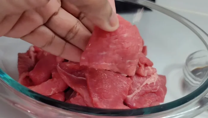 Season the thinly sliced sirloin steak with dark soy sauce, light soy sauce, egg white, corn starch, white pepper, and mushroom seasoning. Chop the steak into bite-sized pieces and set aside.