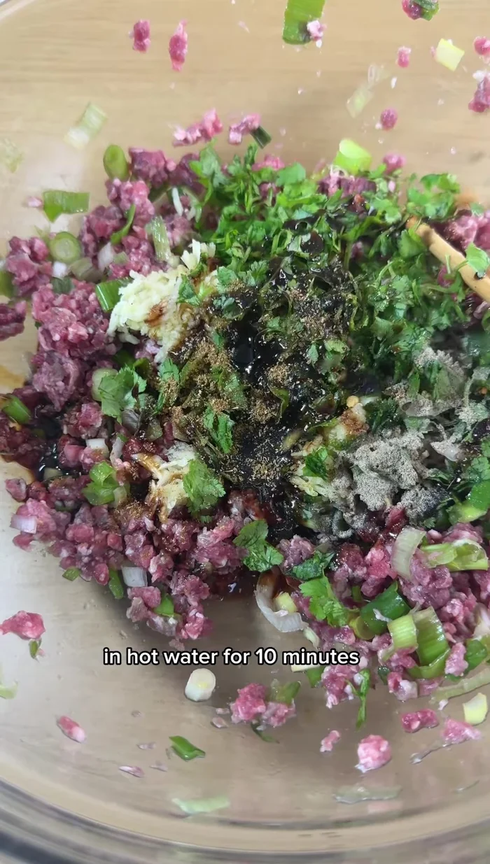 Soak chopped green onions in hot water for 10 minutes. Mix them with minced lamb, ginger, garlic, white pepper, fresh coriander, sweet soy sauce, coriander powder, and chili flakes.