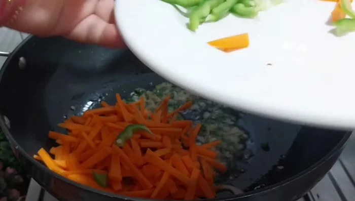 Add chopped onion, carrot, and capsicum. Stir-fry on high heat to maintain crunch.