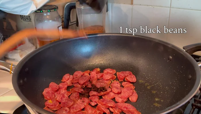 In a hot wok or pan, add the salted beans and then stir in the Chinese sausage.