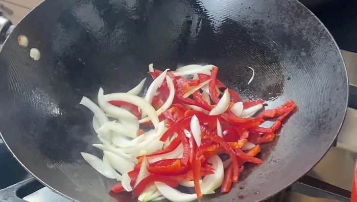 Add vegetable oil, red peppers, white onions, and minced garlic to a wok or pan. Stir-fry for 2 minutes, until the onions soften slightly.