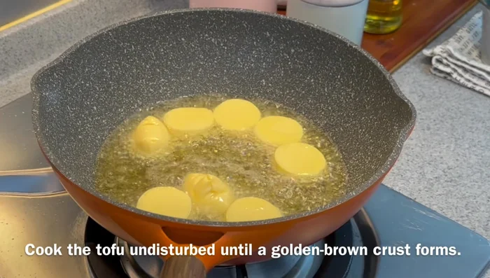 Gently place half of the egg tofu (200g) into the hot oil. Do not move the tofu initially; let a crust form.