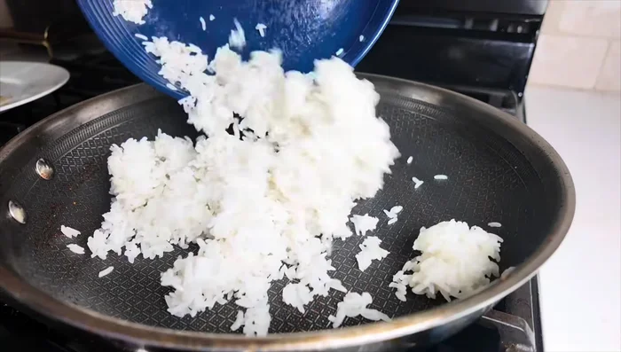 In the same pan, add a little oil, then add cooked rice and stir-fry. Add chopped carrots.
