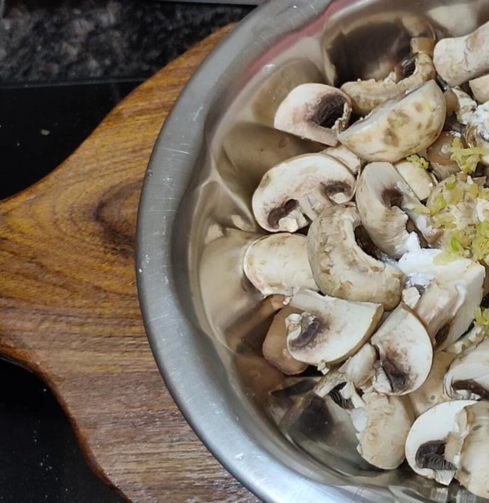 Add grated ginger-garlic (or paste), corn flour, flour, salt, and Schezwan chutney (or red chili-garlic paste) to the mushrooms. Mix well, adding water to coat evenly.