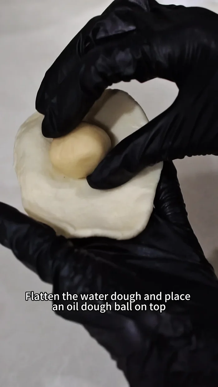 Make the crust: Flatten a water dough piece, place an oil dough piece on top, wrap it into a ball, roll into a long strip, fold and roll up. Rest for 15 minutes.