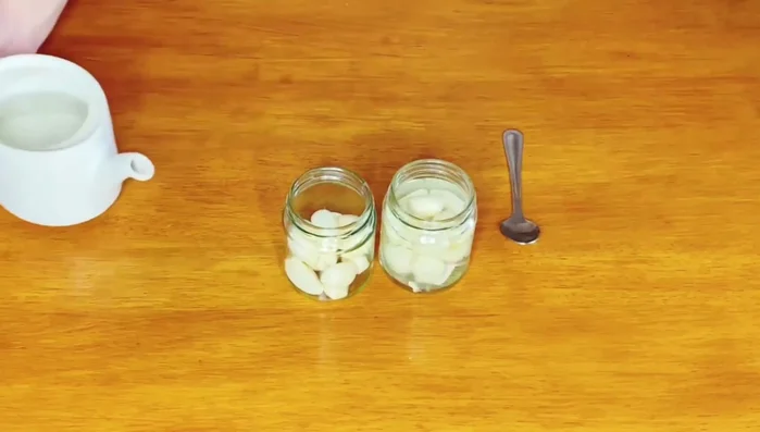 In the other jar, add peeled garlic cloves, 1 teaspoon of salt, 1 teaspoon of sugar, and fill with white vinegar.
