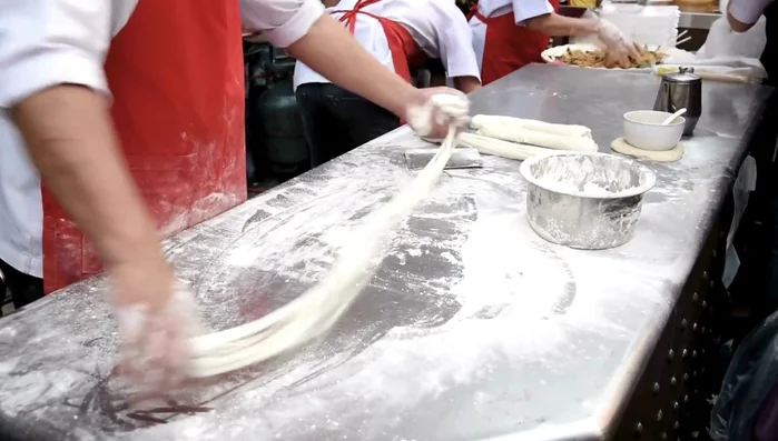 Begin stretching the dough using your hands. Pull, fold, twist, and pull again, using gravity to assist. Flour your surface lightly to prevent sticking.