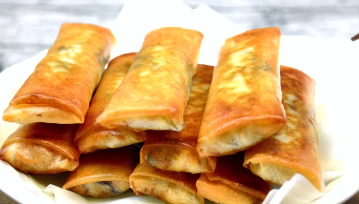 Assemble the spring rolls: Lay a softened wrapper flat. Place a spoonful of the filling in the center. Fold in the sides, then tightly roll from the bottom up.