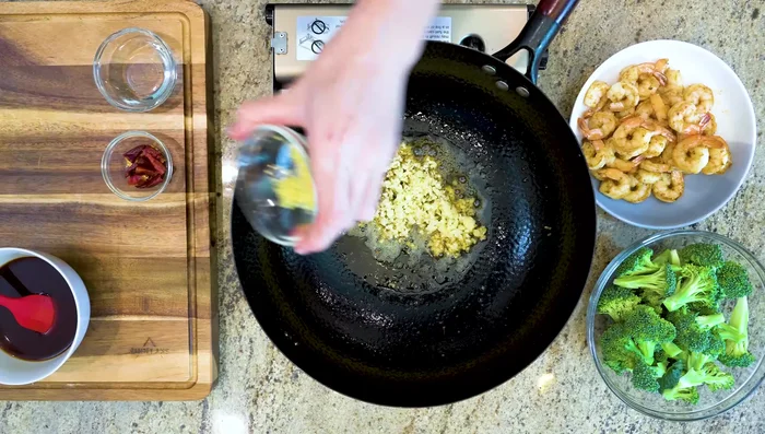 Add garlic, ginger, chilies (optional), and broccoli to the wok. Add a splash of water, cover, and steam for a minute or two.