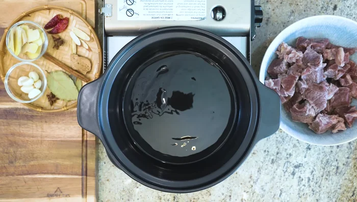 Sauté aromatics: Heat oil in a clay pot. Add garlic, ginger, star anise, bay leaves, cinnamon, orange peel, gan cao (or fennel seeds), goji berries, and red chilies. Stir until garlic is slightly golden.