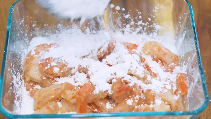 Coat the shrimp in cornstarch: Add half of the remaining cornstarch to a large container. Add the marinated shrimp, then coat with the rest of the cornstarch. Shake well to evenly coat (155.64). Let it sit for 10 minutes (188.879).