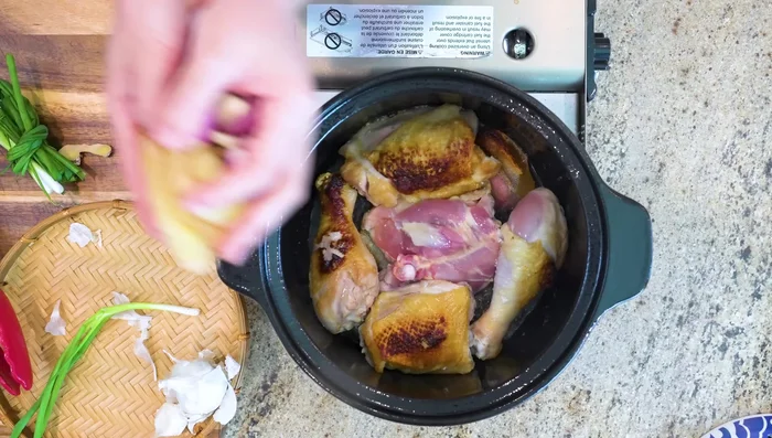 Add aromatics (ginger, garlic, shallots, scallions) between the chicken pieces in the pot.