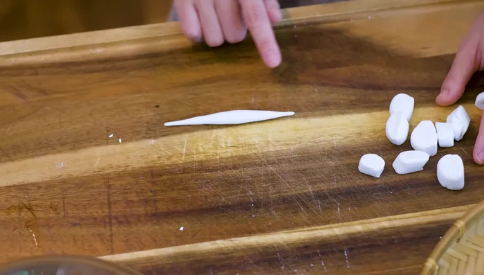 Shape the dough pieces into long, thin noodles by rolling them back and forth between your hands.