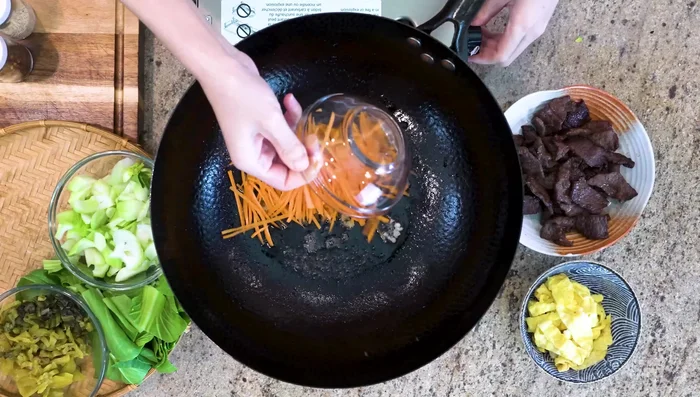 Sauté the garlic, fermented black beans, carrot, pickled mustard green, and bok choy stems in the wok.
