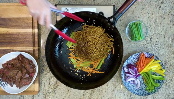 Add the seasoned noodles to the wok and toss with tongs until fluffy.