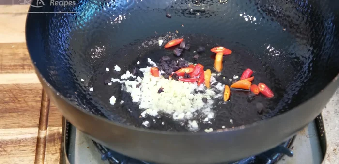 Add minced garlic, ginger, chilies, and fermented black beans to the wok and stir until fragrant.