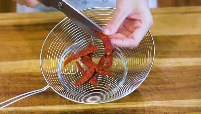 Cut open dried red chilies lengthwise into strips using scissors, removing seeds.