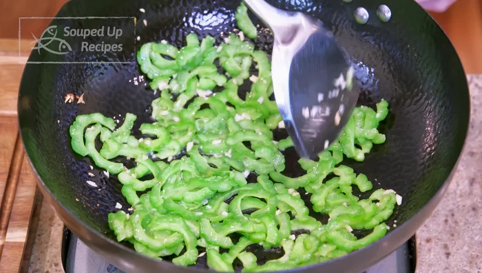 Spread bitter melon in the wok, pour egg over it to cover. Stir; the egg will wrap around the melon slices.