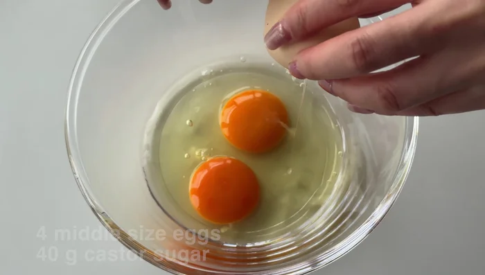 Crack eggs into a bowl, add half the sugar, and squeeze in fresh lemon juice.