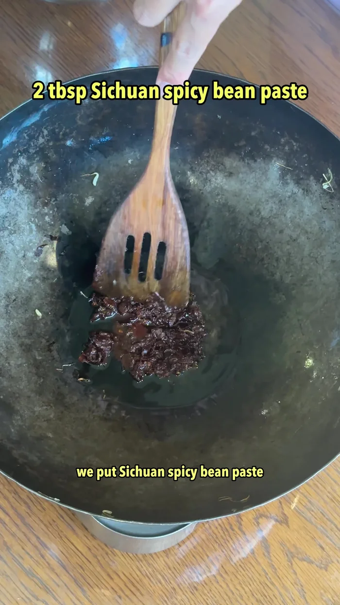 In the pan, add oil, Sichuan spicy bean paste, fermented soybeans, light soy sauce, and a pinch of sugar. Stir-fry.