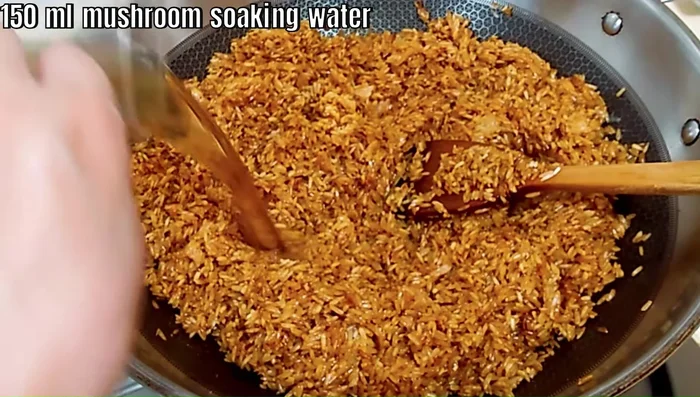 Add 150ml of mushroom soaking water to the rice, stir-frying until slightly sticky.
