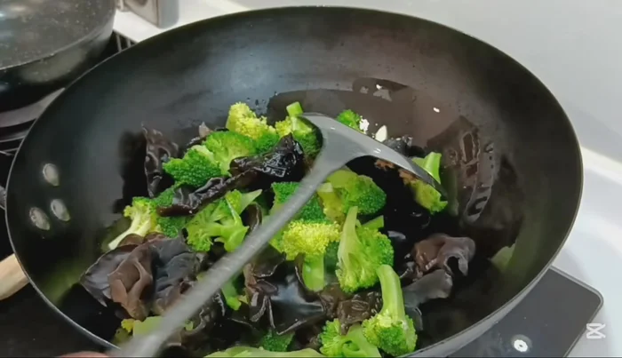 Add the blanched broccoli and wood ear mushrooms to the wok. Stir-fry until heated through.