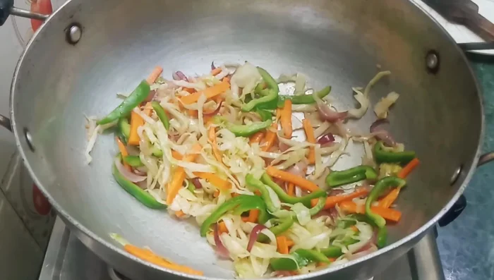 Add the boiled and cooled noodles to the pan. Mix well with the vegetables and spices.