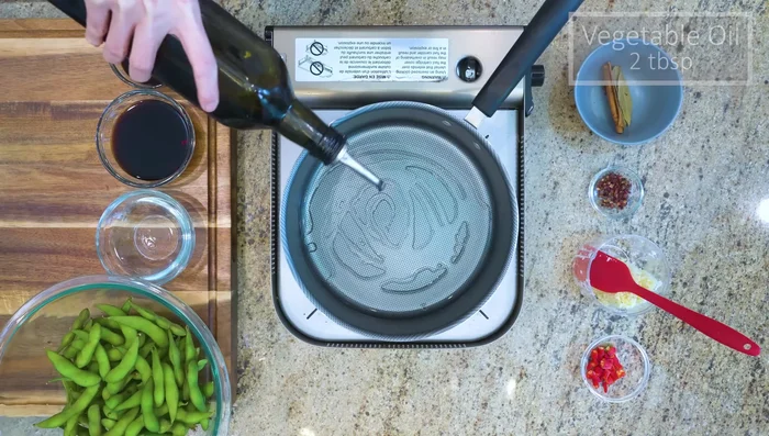 While the edamame cools, prepare the sauce: Heat vegetable oil in a pan. Add cinnamon, bay leaves, star anise, and citron peppercorns. Stir for 1-2 minutes.
