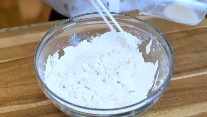 Gradually add flour and stir with chopsticks until a rough dough forms. Scrape the bottom and sides of the bowl.