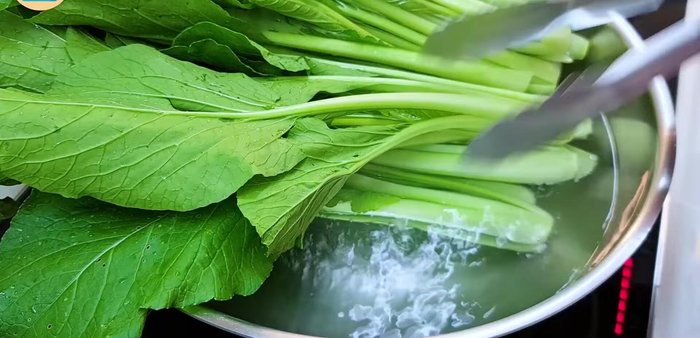Add choy sum to the boiling water, using tongs to submerge completely. Spread them out to cook evenly.
