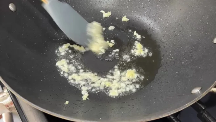 Add minced garlic and grated ginger to the wok and cook briefly.